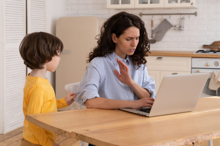 Photo of a woman working on her laptop being interrupted by her child